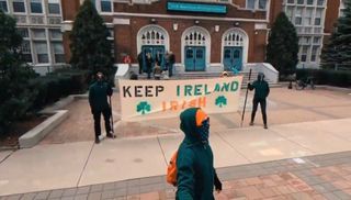 three masked men in sunglasses, green hoodies and orange hates holding banner outside Irish American Heritage Center. it reads keep ireland irish and has shamrocks