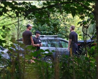three men in matching black t shirts and athletic shorts. two are wearing baseball caps
