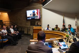 Four police officers in front row seating look on as village trustees at round desk hold meeting