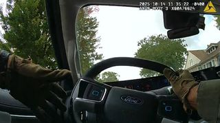 The driver's two gloved hands are visible, one is on the steering wheel. The speedometer reads 51 mph. Trees and homes are visible through the windshield.