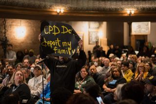 A man stands up amid a crowd, holding a sign that reads "CPD don't deport my family."