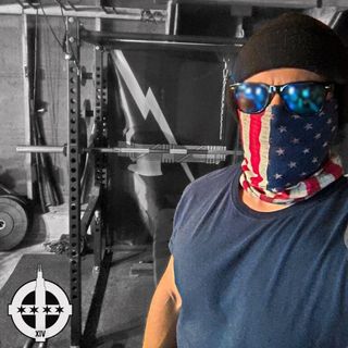 man posing in front of gym equipment. he is wearing an american flag face mask, black beanie and sunglasses