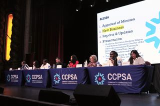 Seven CCPSA commissioners and their executive director sitting behind a long table with slides projected on the screen behind.