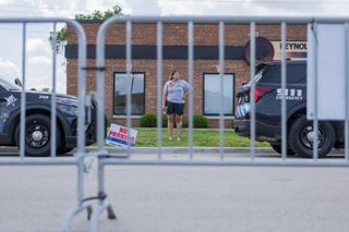 A woman standing outside a brick building with a security fence in the foreground.
