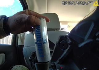 The point of view is the rear driver-side seat of an SUV. A man's left hand inserts a silver canister with blue print reading "CM | MUZZLEBLAST | CS" into his launcher.