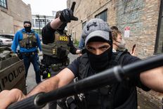 close up of masked ICE agent in an alley pushing back against viewer/photographer with a baton