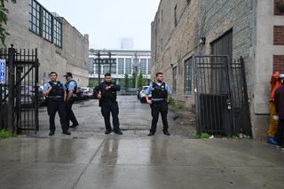 four police officers in blue uniform shirts standing in front of alley