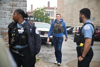 foreground: two cpd officers in blue uniform shirts
background: HSI agent in olive body armor carrier and blue hoodie