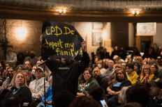 A man stands up amid a crowd, holding a sign that reads "CPD don't deport my family."