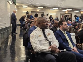Superintendent Snelling dressed in white shirt and black pants sits in the front row with members oft eh public seated behind him.